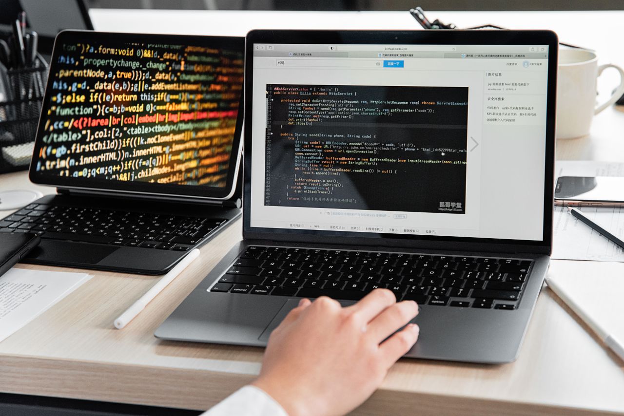 hero-img A developer writing code on a laptop, displaying programming scripts in an office environment.